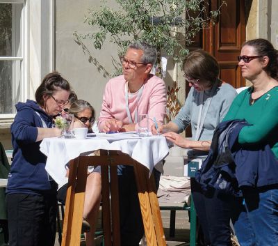 Eine Gruppe von Menschen sitzt bei schönem Wetter draußen und ist beschäftigt mit Schreibarbeiten.