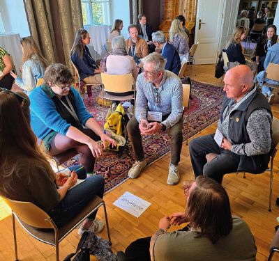 Personen sitzen in einem Kreis auf Stühlen und diskutieren bei einer Veranstaltung.