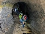 Blick von unten in einen dunklen Stollen. Mehrere Personen erklimmen eine schmale, holzgebaute Treppe.