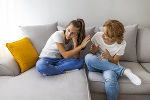 Mutter sitzt erklärend und das Gespräch suchend mit ihrer Tochter auf der Couch, diese hat eine ablehnende Handhaltung und blickt in die entgegengesetzte Richtung. Mutter sitzt erklärend und das Gespräch suchend mit ihrer Tochter auf der Couch, diese hat eine ablehnende Handhaltung und blickt in die entgegengesetzte Richtung.