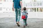 Kind mit einem Rucksack, welches von einer erwachsenen Person an der Hand geführt wird. Kind mit einem Rucksack, welches von einer erwachsenen Person an der Hand geführt wird.