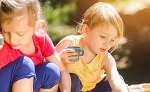 Zwei Kinder spielen konzentriert im Freien. Sie sitzen nebeneinander und beschäftigen sich mit kleinen Spielsachen.