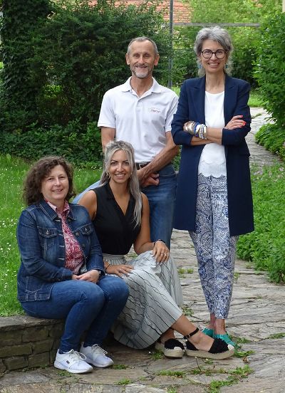 Gruppe von vier Menschen im Garten. Eine Person sitzt, die anderen stehen. Im Hintergrund üppige Vegetation.