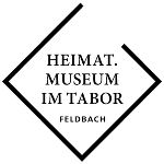 LOGO des Museum im Tabor Feldbach mit der Aufschrift HEIMAT. MUSEUM IM TABOR FELDBACH. Weißer Htergrund mit schwarzen Schriftzügen.