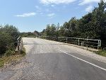 Blick auf eine Asphaltstraße, die über eine Brücke führt. Begrenzt von Bäumen und Büschen an beiden Seiten.