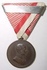 Bronze, Hersteller: Stempelschneider Tautenhayn, mit Ringöse am originalen Dreiecksband und Wiederholungsspange für die 2. Verleihung.