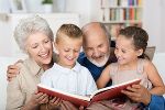 Symbolbild von Großeltern mit ihren Enkelkindern auf dem Schoß, es wird gemeinsam ein Buch angeschaut.