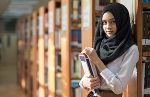 Symbolbild von einem Mädchen mit Kopftuch, welches an einem Bücherregal lehnt. Symbolbild von einem Mädchen mit Kopftuch, welches an einem Bücherregal lehnt.