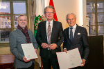 Alfred Haidacher (l.) und Dieter Pochlatko (r.) mit LH Christopher Drexler (M.) stehend nebeneinander in der Aula der Alten Universität.