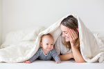 Eine Mutter liegt mit ihrem Kleinkind am Boden, über beide ist eine Decke gebreitet. Eine Mutter liegt mit ihrem Kleinkind am Boden, über beide ist eine Decke gebreitet.