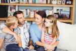 Symbolbild in Form einer Familie mit zwei Erwachsenen und zwei Kindern, die auf einer Couch sitzen und etwas besprechen. Symbolbild in Form einer Familie mit zwei Erwachsenen und zwei Kindern, die auf einer Couch sitzen und etwas besprechen.