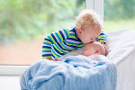 Symbolbild in Form von einem schlafenden Baby und einem Kleinkind, das sich darüber beugt und den Säugling auf den Kopf küsst.