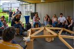 Mehrere Personen sitzen um eine Holzkuppel bei der Veranstaltung "Inklusive Caring Communities", ein Mann spricht in ein Mikrophon. © Mark Staskiewicz